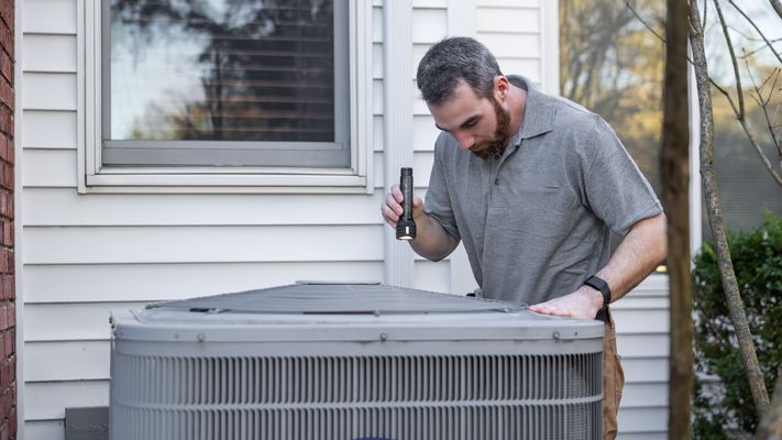A technician inspects an outdoor air conditioning unit